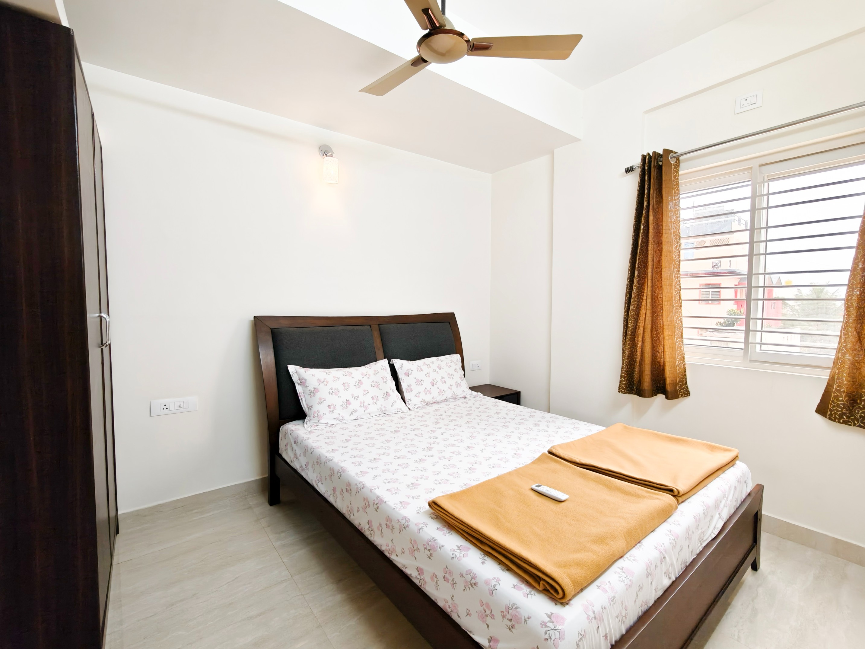 Bright Classica studio apartment featuring white walls, ceiling fan, modern furnishings, comfortable bed with floral bedding, and golden curtains